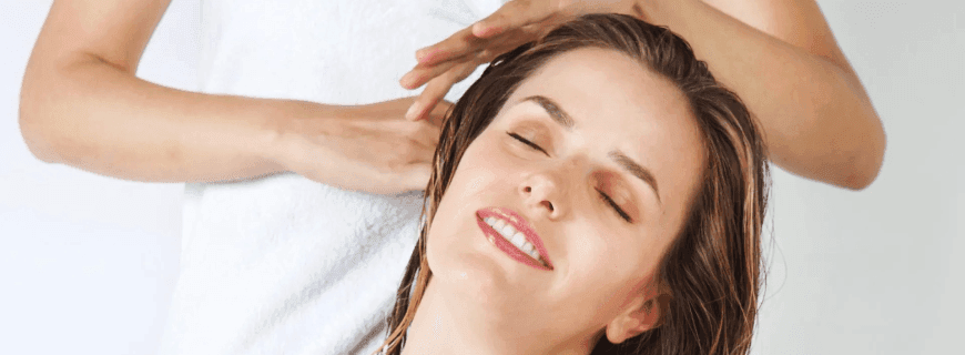 Donna con i capelli bagnati e un'espressione rilassata mentre riceve un trattamento ai capelli in un salone di bellezza.