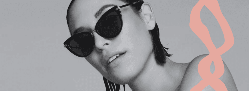 Modella che indossa occhiali da sole neri con montatura elegante, in uno sfondo minimalista e monocromatico.