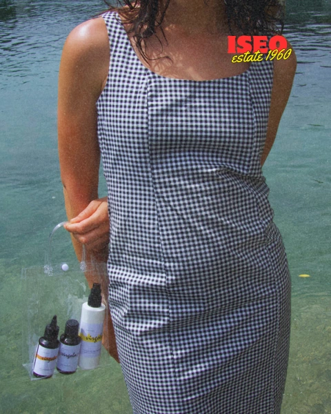 Abito a scacchi indossato da una persona con una borsa trasparente contenente prodotti per la cura dei capelli, sullo sfondo di un'acqua blu.