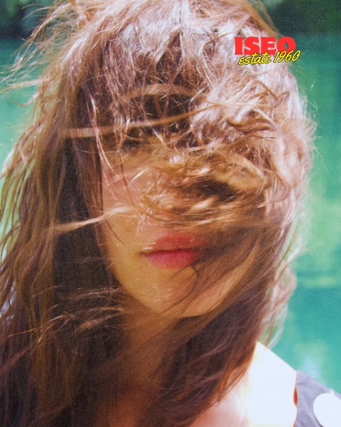 Ritratto di una donna con capelli lunghi e mossi, coperti da una leggera brezza, che nasconde parzialmente il viso.