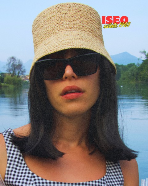 Donna con cappello di paglia e occhiali da sole, in primo piano, con sfondo naturale e acqua. Logo ISEO visibile in alto a destra.