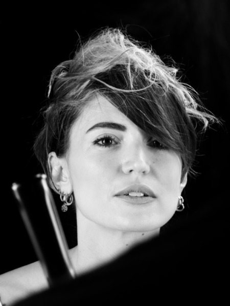 Ritratto in bianco e nero di una donna con capelli disordinati e orecchini, che guarda verso la fotocamera.