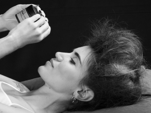 Modella con capelli voluminosi che tiene un barattolo di prodotto per capelli, in un'illuminazione morbida e contrasto in bianco e nero.